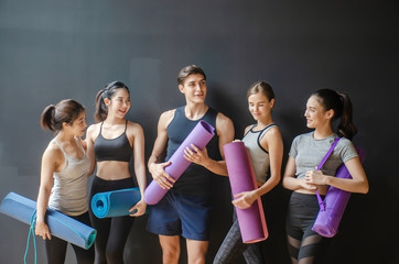 Group of young sporty people with fitness yoga exercise mats standing beside black wall.Students taking a rest from fitness activity, waiting for a lesson to start in loft studio