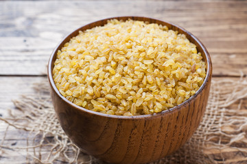 Traditional Turkish dry raw bulgur cereal in a wooden bowl.