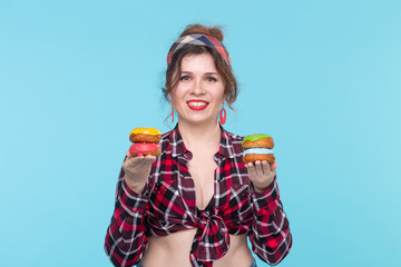 Positive young pin-up girl model holding in hands multicolored donuts posing on a blue background....