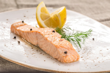 Steamed salmon with lemon on white plate on grey tablecloth