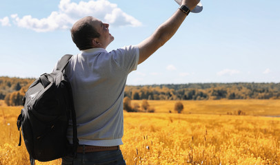 A young man is traveling in nature. Traveling with a backpack on the shoulders of a beautiful park. Hitchhiking with one bag in autumn.
