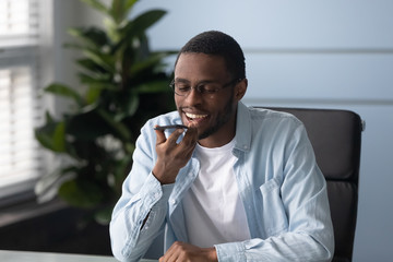 Happy millennial african american male worker recording voice message.