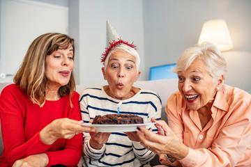 Group of seniors celebrating a birthday in the retirement house. Seniors on birthday at home. Senior woman blowing out candles on cake. Senior Life Celebration Cake Birthday..