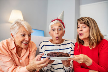 Group of seniors celebrating a birthday in the retirement house. Seniors on birthday at home. Senior woman blowing out candles on cake. Senior Life Celebration Cake Birthday..