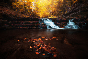Beautiful waterfall at mountain river in colorful autumn forest with red and orange leaves at sunset. Nature landscape