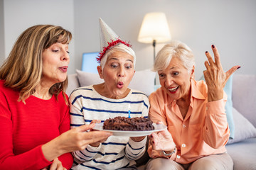 Senior Life Celebration Cake Birthday. Birthday surprise party.Happy mature women celebrating birthday at home. Senior woman blow on birthday cake during a birthday party