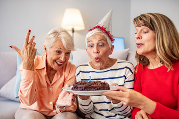 Senior Life Celebration Cake Birthday. Birthday surprise party.Happy mature women celebrating birthday at home. Senior woman blow on birthday cake during a birthday party