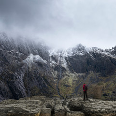 Fototapeta na wymiar Stunning dramatic landscape image of snowcapped Glyders mountain range in Snowdonia during Winter with menacing low clouds hanging at the peaks