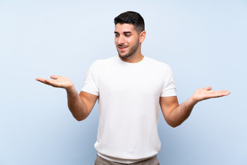 Caucasian handsome man over isolated blue background holding copyspace with two hands