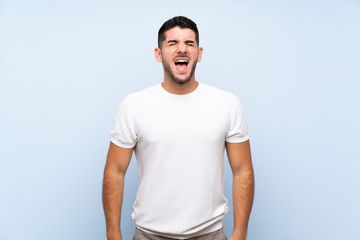 Caucasian handsome man over isolated blue background shouting to the front with mouth wide open