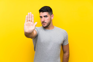 Young handsome man over isolated yellow background making stop gesture with her hand