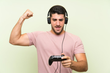 Young handsome man playing with a video game controller over isolated green wall celebrating a victory