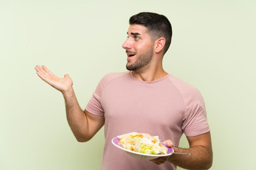 Young handsome man with salad over isolated green wall with surprise facial expression