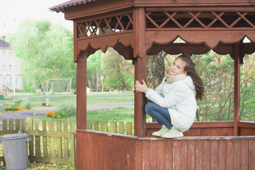 Cute girl in down jacket sitting on gazebo on an autumn day.