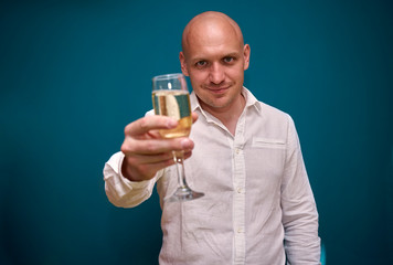 handsome man stands with a glass of champagne against a blue wall