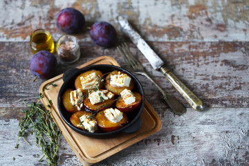 Selective focus. Macro. Baked plums with feta cheese in a cast iron skillet with herbs.