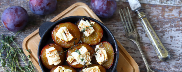 Selective focus. Macro. Baked plums with feta cheese in a cast iron skillet with herbs.