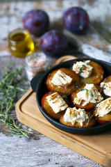 Selective focus. Macro. Baked plums with feta cheese in a cast iron skillet with herbs.