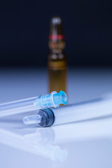 Pen medical syringe, ampule with saline and vial with dry human hormone drug powder, forbidden sportsmen doping. Blue syringe with bare needle lying on saline ampule. Macro image.