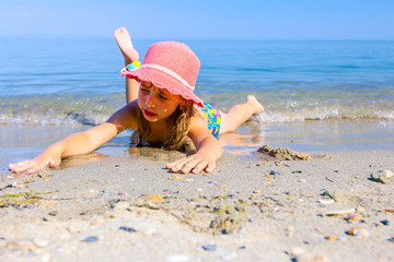 Child girl with summer hat is lying on the stomach in shallow sea water