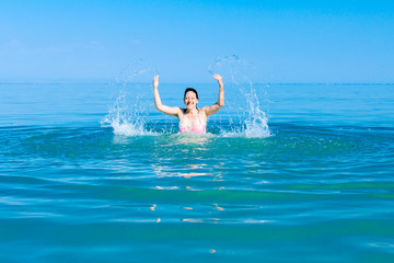 Excited female jumping with widespread hands in shallow sea water