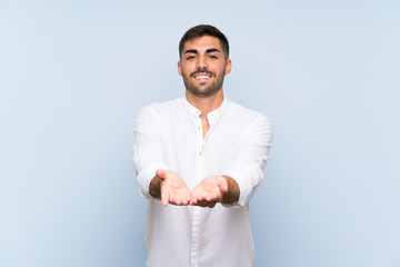 Handsome man with beard over isolated blue background holding copyspace imaginary on the palm to...
