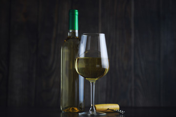 Fototapeta na wymiar Transparent bottle of white dry wine on the table. White wine glass on a wooden background.
