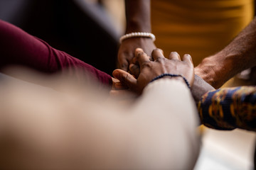 Point of view, diverse business people putting their hands on top of each other wearing casual clothes and african patterns.