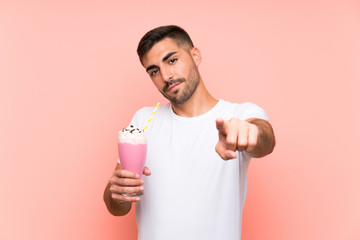 Young man with strawberry milkshake over isolated pink background points finger at you with a confident expression