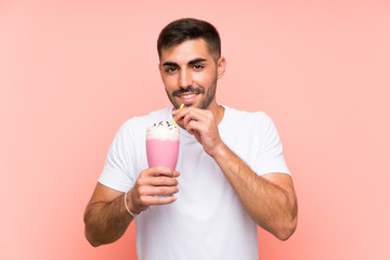 Young man with strawberry milkshake over isolated pink background