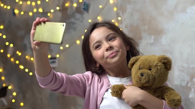 Little girl alone in room taking selfie photos hugging teddy