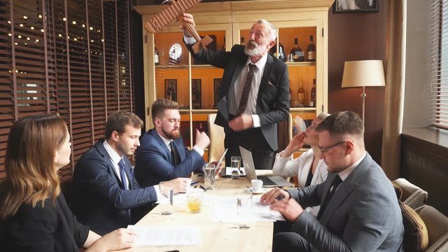 Elderly team leader dressed in business suit demonstrates the layout of helicopter to business partners. Young men carefully studying documentation, businesswoman watching speaker with interest