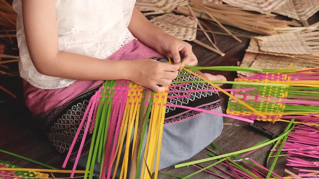 Girl with folk costume weave colorful pieces of bamboo or basketry to get locally style fan.