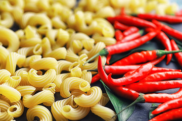 Uncooked pasta on a stone background. With seasonings and spices, spicy chili peppers.