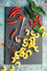 Uncooked pasta on a stone background. With seasonings and spices, spicy chili peppers.