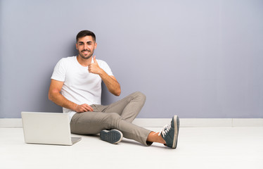 Young man with his laptop sitting one the floor giving a thumbs up gesture