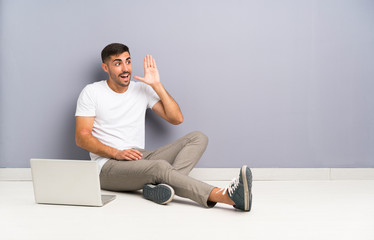 Young man with his laptop sitting one the floor shouting with mouth wide open