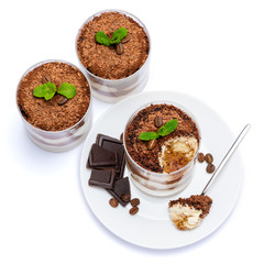 Classic tiramisu dessert in a glass cup on the plate and pieces of chocolate on white background with clipping path