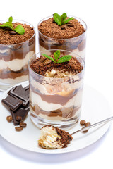 Classic tiramisu dessert in a glass cup on the plate and pieces of chocolate on white background with clipping path