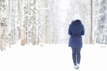 A young girl in a winter park on a walk. Christmas holidays in the winter forest. The girl enjoys winter in the park.