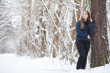 A young girl in a winter park on a walk. Christmas holidays in the winter forest. The girl enjoys winter in the park.