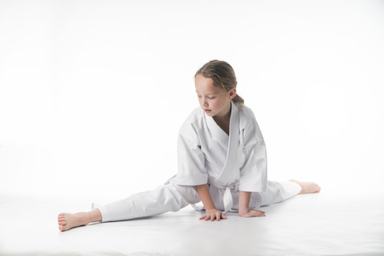 little karate girl in a white kimono and a  belt sits for a workout in sports twine