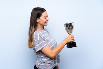 Young brunette woman over isolated blue background holding a trophy