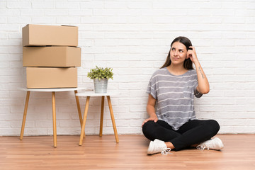 Young woman moving in new home among boxes having doubts and with confuse face expression