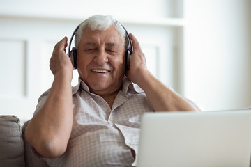 Senior man wearing headphones listens songs on laptop
