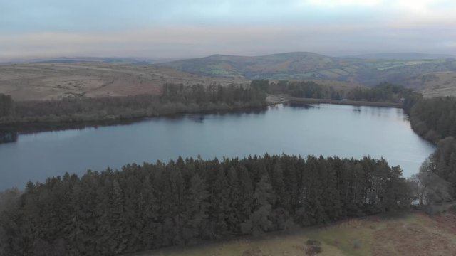 Aerial drone shot of lake surrounded by evergreen trees in winter