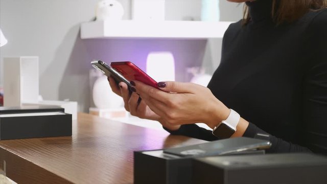 Young unrecognizable woman comparing a two smartphones in an electronics store, close-up hands.