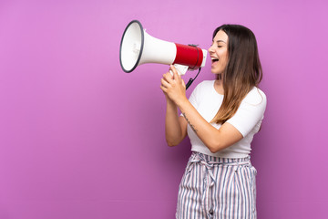 Young woman over isolated purple background shouting through a megaphone