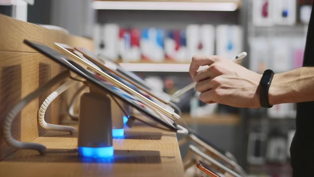 Young unrecognizable man chooses a tablet in an electronics store, close-up. He trying using it with stylus.