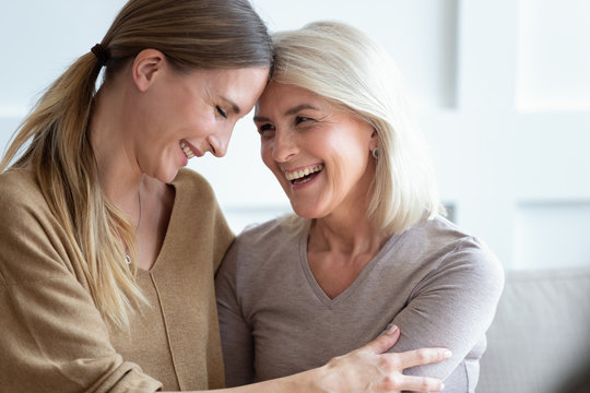 Closeup image aged mother and adult daughter touch foreheads laughing